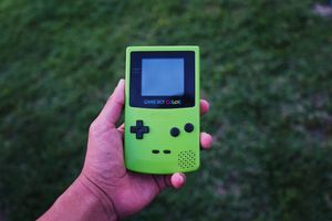 A green gameboy color held in a hand and clipped into an arrow